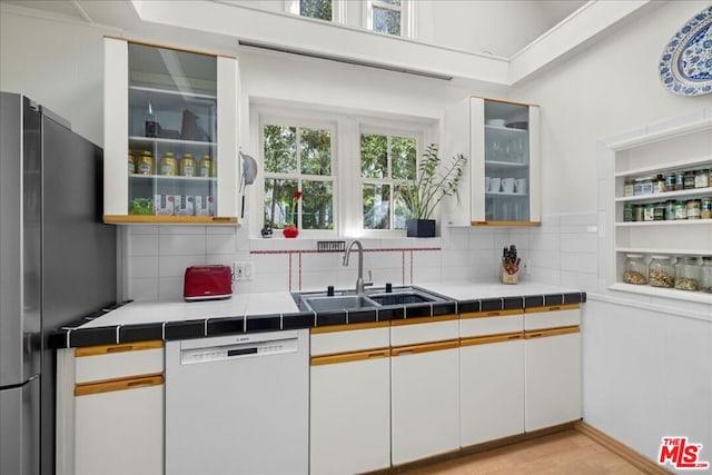 kitchen with sink, stainless steel fridge, tile counters, dishwasher, and white cabinets