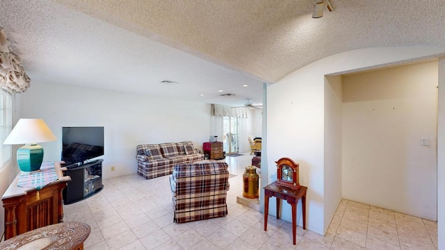 living room with ceiling fan, vaulted ceiling, and a textured ceiling