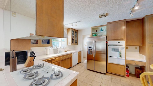 kitchen with sink, white appliances, tile counters, and a textured ceiling