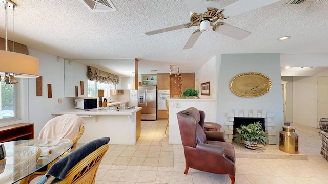 tiled living room featuring ceiling fan, a fireplace, and a textured ceiling