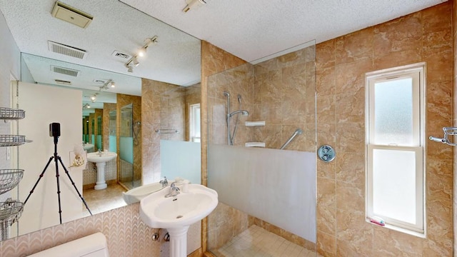 bathroom featuring a tile shower, sink, tile walls, toilet, and a textured ceiling