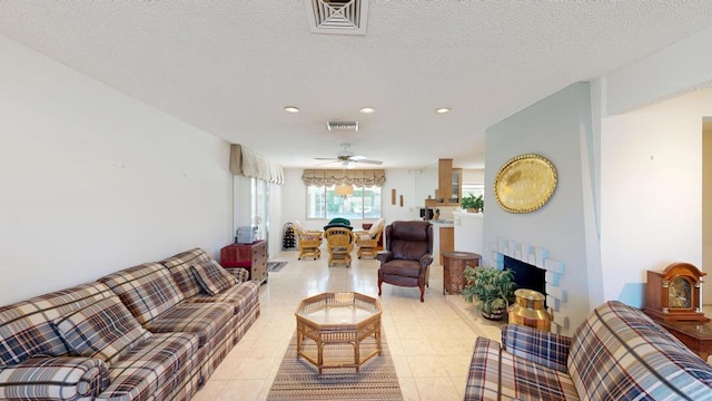 living room featuring light tile patterned flooring, a brick fireplace, ceiling fan, and a textured ceiling