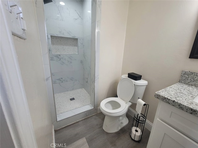 bathroom with hardwood / wood-style flooring, vanity, tiled shower, and toilet