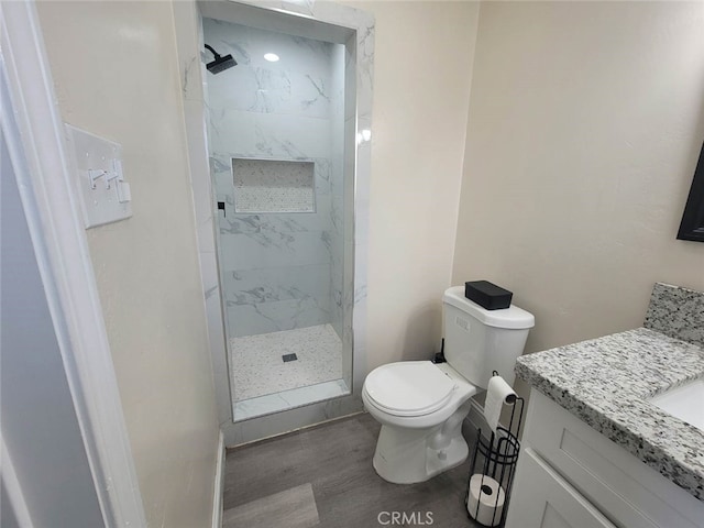 bathroom with vanity, hardwood / wood-style flooring, toilet, and a tile shower