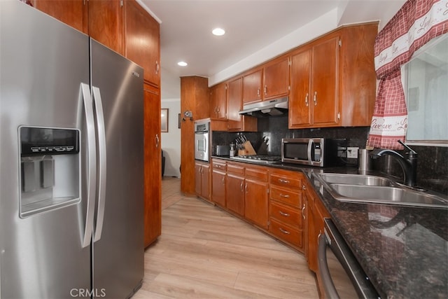 kitchen with sink, tasteful backsplash, dark stone counters, stainless steel appliances, and light hardwood / wood-style floors