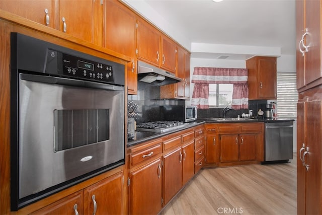 kitchen with stainless steel appliances, sink, decorative backsplash, and light hardwood / wood-style flooring