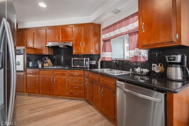 kitchen with appliances with stainless steel finishes, tasteful backsplash, sink, dark stone counters, and light wood-type flooring