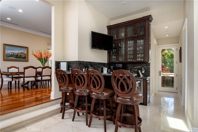 bar with tasteful backsplash, ornamental molding, and dark brown cabinets