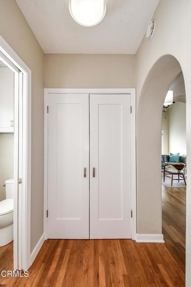 corridor featuring arched walkways, baseboards, and wood finished floors