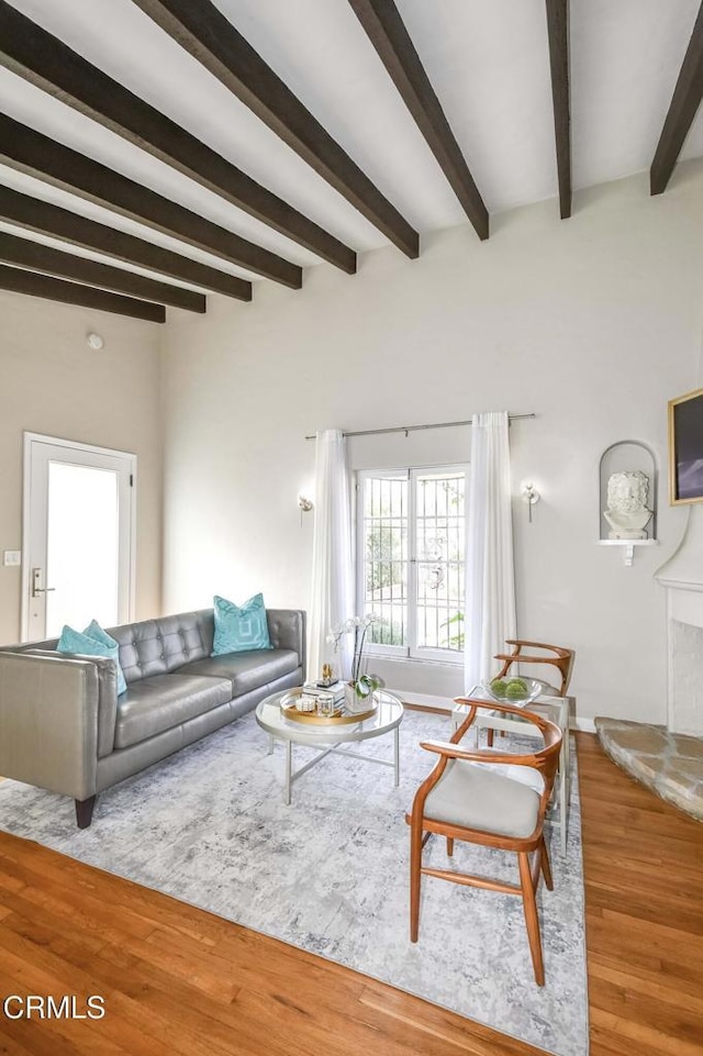 living area featuring light wood-style floors, a fireplace with raised hearth, and beamed ceiling