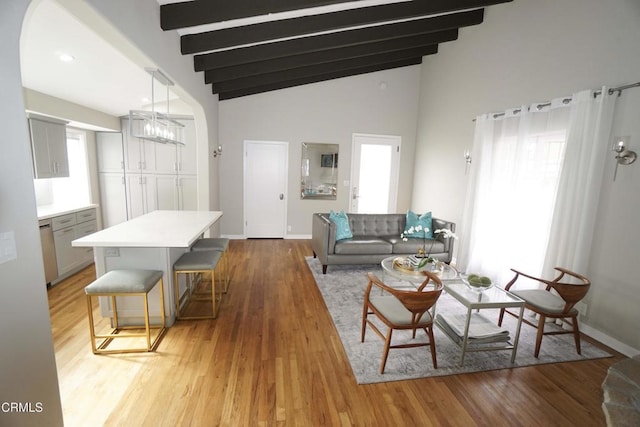 living area with a healthy amount of sunlight, baseboards, lofted ceiling with beams, and light wood finished floors