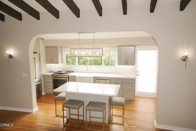 kitchen with arched walkways, stainless steel appliances, a breakfast bar, light countertops, and a center island