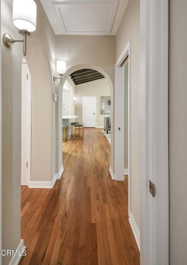 corridor featuring arched walkways, baseboards, and wood finished floors