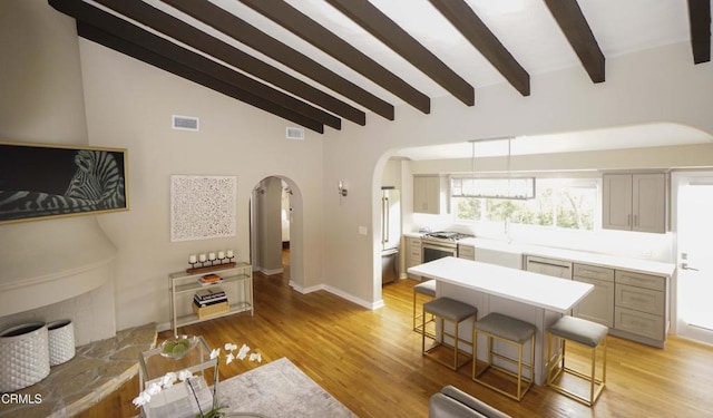 living area with vaulted ceiling with beams, light wood-style flooring, visible vents, and arched walkways