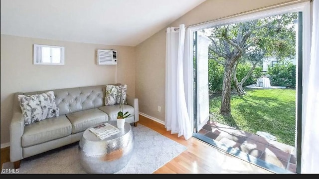 living room with lofted ceiling, a wall mounted AC, wood finished floors, and baseboards