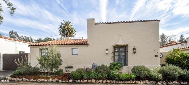 view of front facade featuring a tile roof, fence, a chimney, and stucco siding