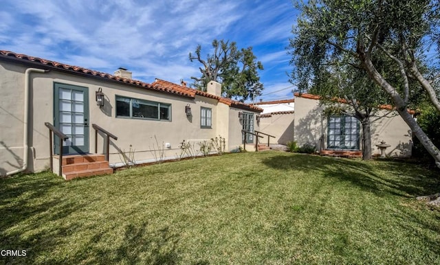 back of property featuring a tile roof, a yard, a chimney, stucco siding, and entry steps