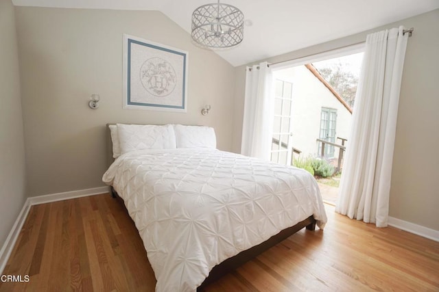 bedroom featuring access to outside, lofted ceiling, baseboards, and wood finished floors