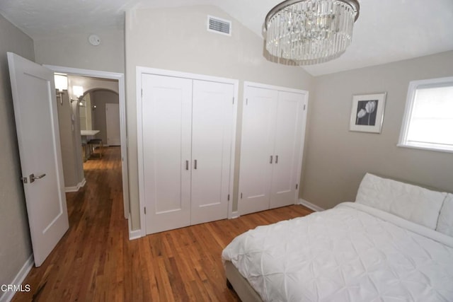 bedroom with arched walkways, wood finished floors, visible vents, vaulted ceiling, and two closets