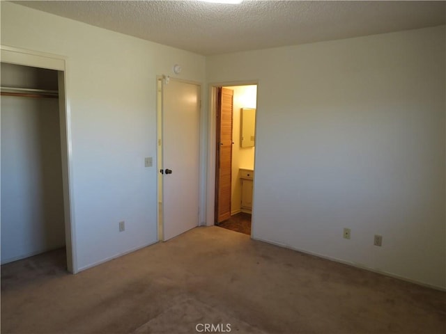 unfurnished bedroom with ensuite bath, a closet, a textured ceiling, and carpet flooring