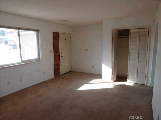 unfurnished bedroom with multiple closets, light colored carpet, and a textured ceiling