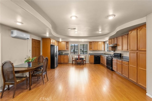 kitchen with sink, a wall mounted air conditioner, a tray ceiling, black appliances, and light wood-type flooring