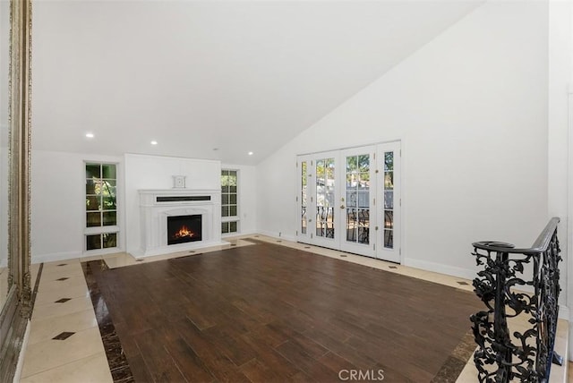 unfurnished living room featuring high vaulted ceiling, light hardwood / wood-style floors, and french doors