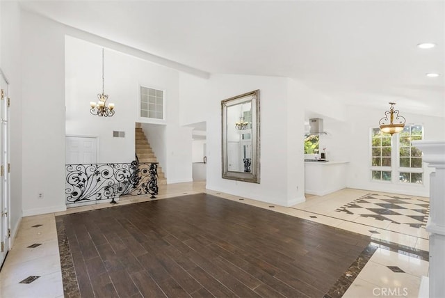 unfurnished living room featuring a notable chandelier, high vaulted ceiling, and light hardwood / wood-style flooring