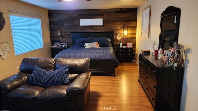 bedroom with ceiling fan, light hardwood / wood-style floors, and wood walls