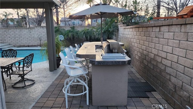 view of patio / terrace featuring a fenced in pool, grilling area, an outdoor bar, and exterior kitchen