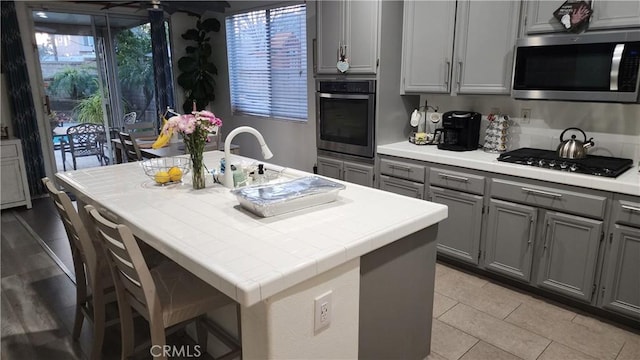 kitchen featuring appliances with stainless steel finishes, gray cabinets, a kitchen island with sink, and sink