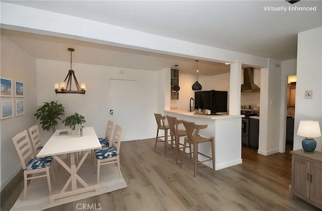 kitchen with refrigerator, stainless steel range with electric stovetop, a kitchen breakfast bar, decorative light fixtures, and wall chimney exhaust hood