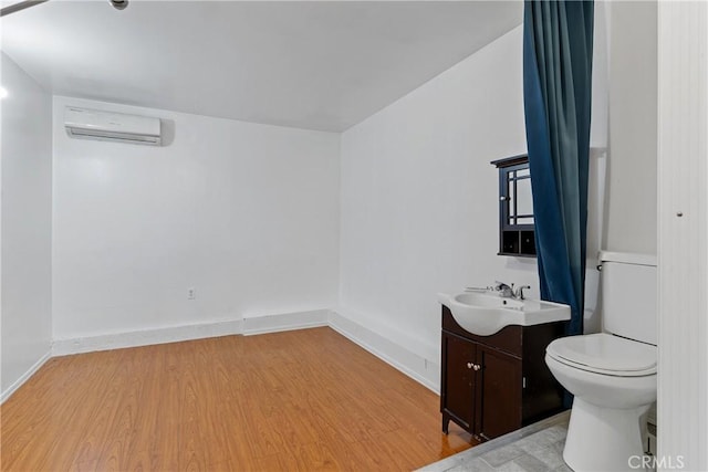 bathroom with toilet, vanity, wood finished floors, a wall mounted air conditioner, and baseboards