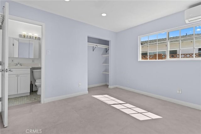 unfurnished bedroom featuring connected bathroom, a sink, baseboards, a closet, and a wall mounted air conditioner