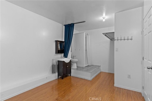 interior space featuring a stall shower, baseboards, toilet, wood finished floors, and vanity