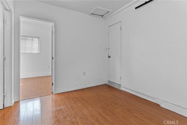 unfurnished room with attic access, light wood-style floors, and baseboards