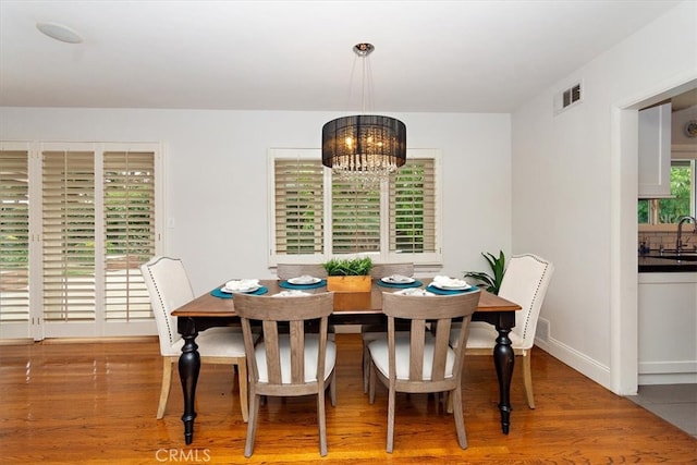 dining room featuring baseboards, wood finished floors, visible vents, and a notable chandelier