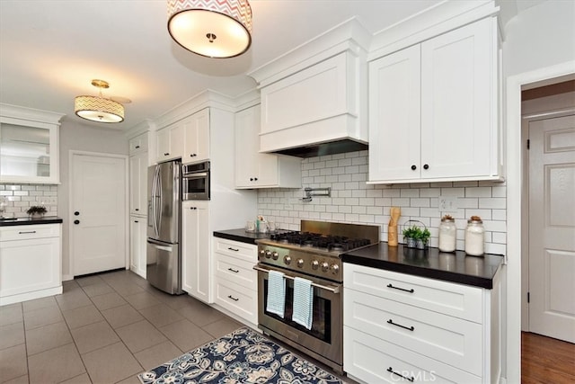 kitchen with white cabinets, appliances with stainless steel finishes, decorative backsplash, dark countertops, and glass insert cabinets