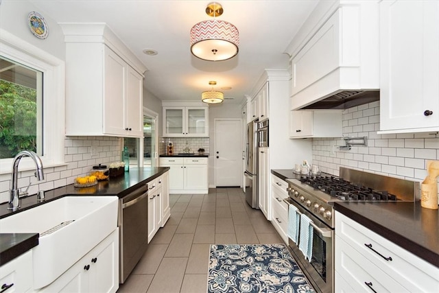 kitchen featuring stainless steel appliances, dark countertops, backsplash, white cabinetry, and a sink