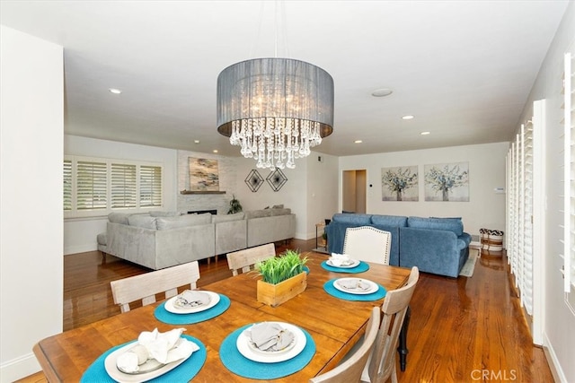 dining space featuring an inviting chandelier, a fireplace, wood finished floors, and recessed lighting