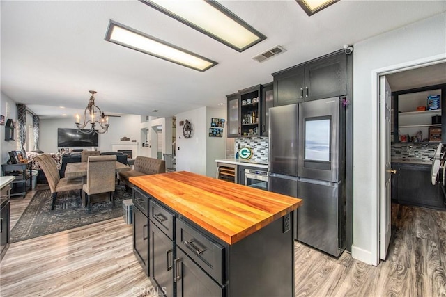 kitchen featuring wood counters, stainless steel refrigerator, a kitchen island, light hardwood / wood-style floors, and decorative backsplash