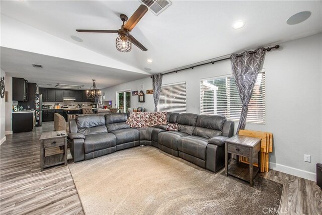 living room with lofted ceiling, wood-type flooring, and ceiling fan with notable chandelier