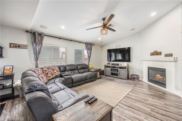 living room featuring a tile fireplace, vaulted ceiling, wood-type flooring, and ceiling fan