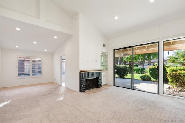 unfurnished living room with a brick fireplace, light colored carpet, and high vaulted ceiling