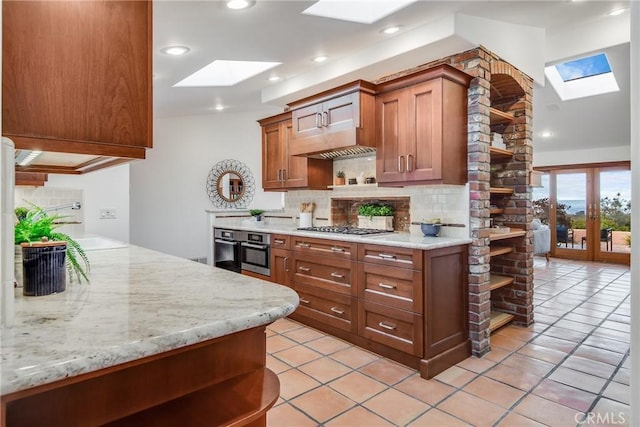 kitchen with light stone counters, appliances with stainless steel finishes, a skylight, and backsplash