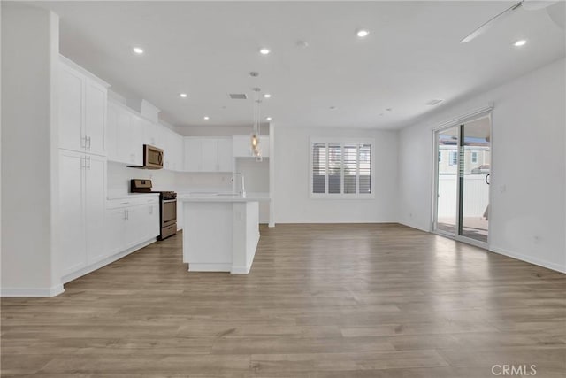 kitchen featuring white cabinetry, a center island with sink, hanging light fixtures, and stainless steel appliances