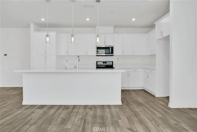 kitchen with white cabinets, hanging light fixtures, a kitchen island with sink, and stainless steel appliances