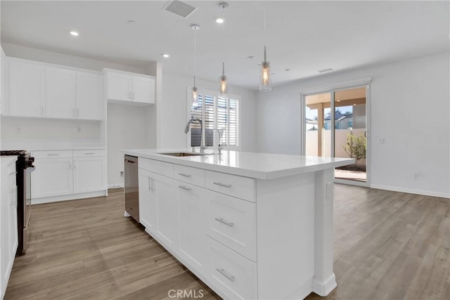 kitchen with sink, hanging light fixtures, stainless steel appliances, white cabinets, and an island with sink