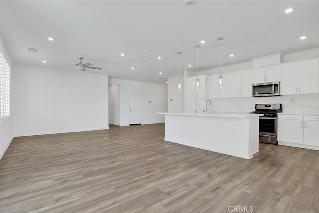 kitchen with appliances with stainless steel finishes, an island with sink, decorative light fixtures, light wood-type flooring, and white cabinetry