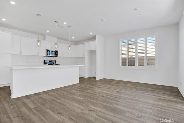 kitchen featuring white cabinetry, a kitchen island with sink, hanging light fixtures, light hardwood / wood-style floors, and appliances with stainless steel finishes